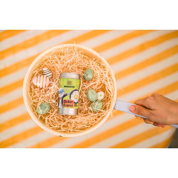 Photo with Easter egg sprinkler in pan with Easter eggs and yellow and white background.